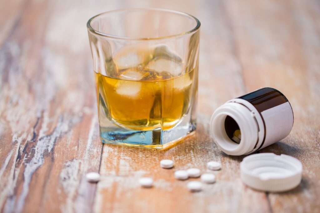 A glass with al alcoholic drink next to a bottle spilling pills, representing how one can benefit from calling a Portland criminal defense attorney.