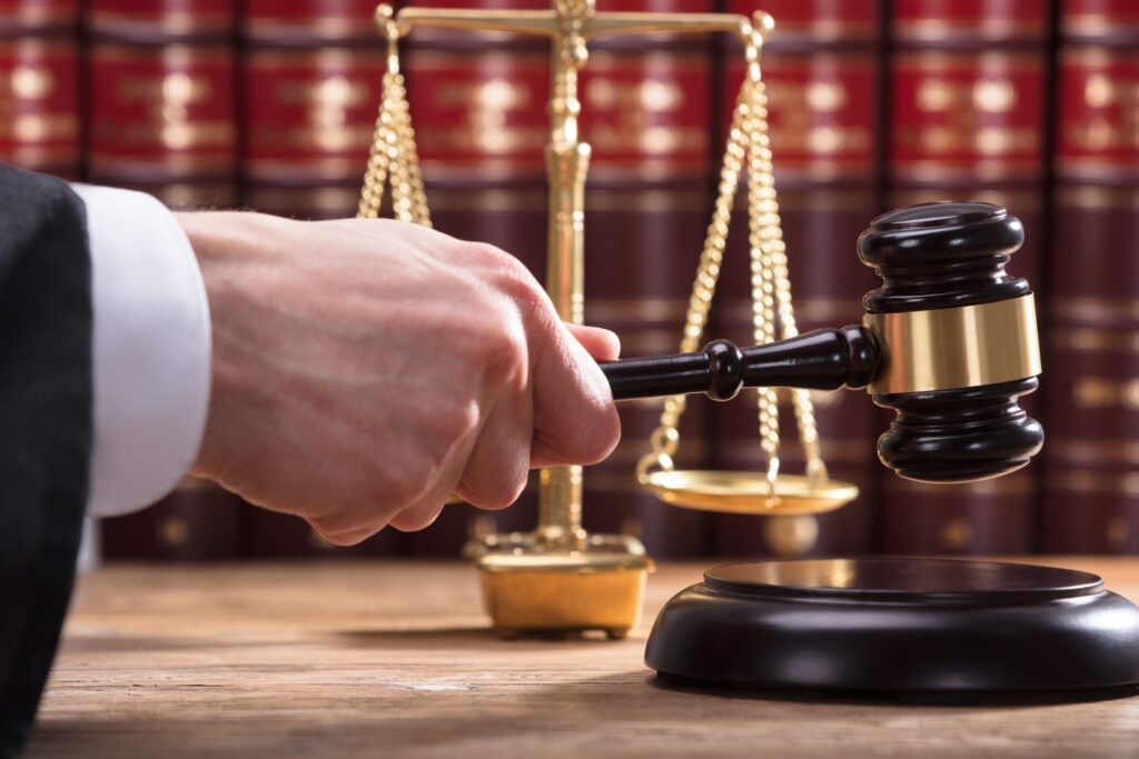 A judge hitting a block with gavel, with a golden scale and books in the background, representing how one can benefit from calling a Portland criminal defense attorney.