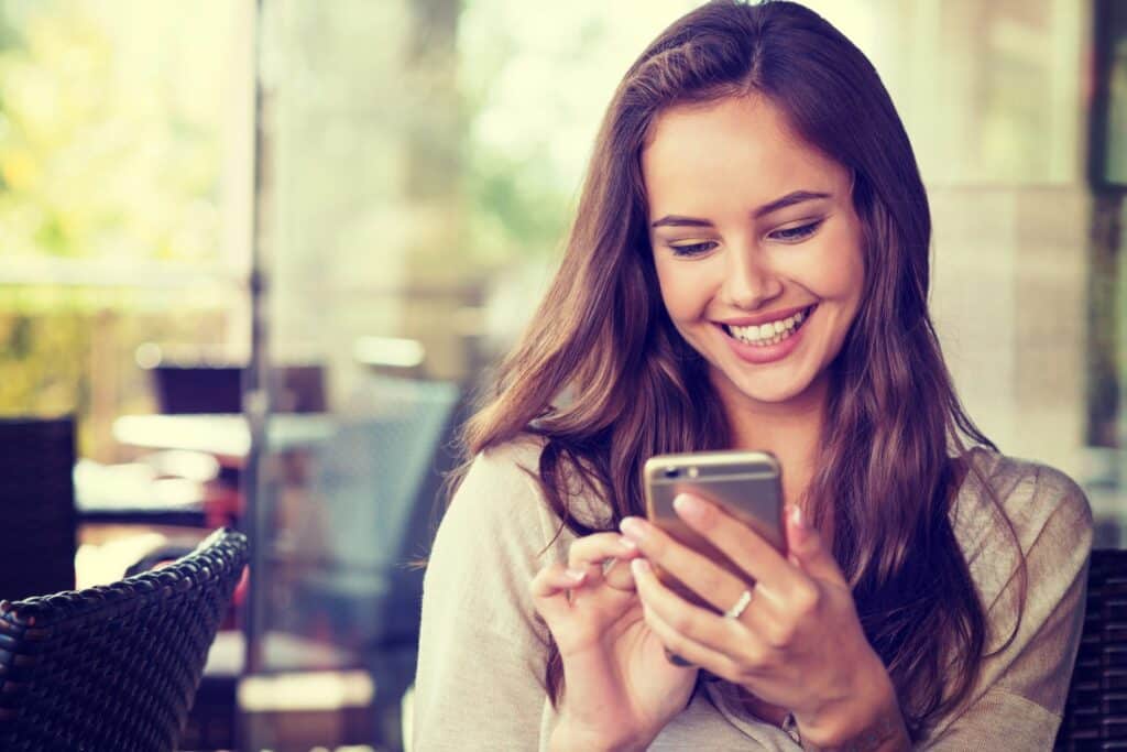 A woman with brown hair in a cafe using her phone and smiling, representing how one can benefit from calling a Portland criminal defense attorney.