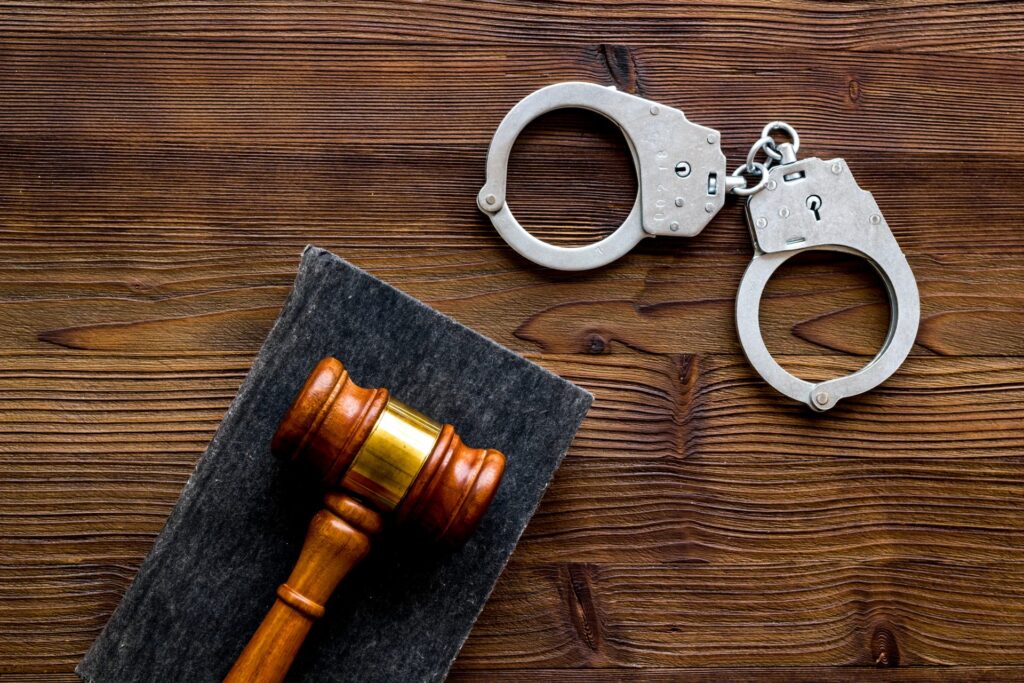 Over a wooden background there are a set if handcuffs and a wooden gavel, representing how one can benefit from calling a Portland criminal defense attorney.
