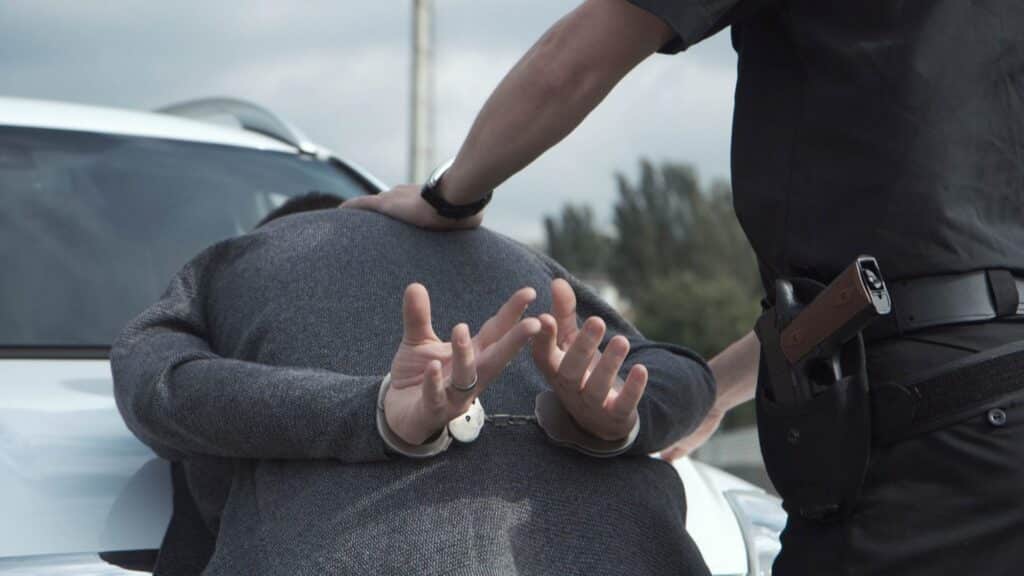 A man being arrested by a police officer against a car, representing how one can benefit from calling a Portland criminal defense attorney.