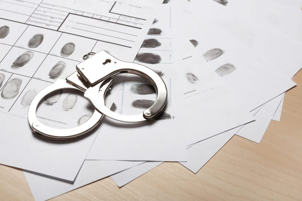 A set of handcuffs on top of several papers with inked fingerprints, representing how one can benefit from calling a Portland criminal defense lawyer.