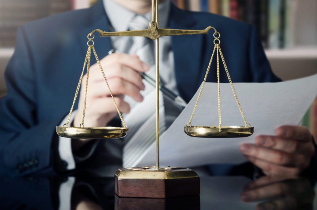 A lawyer with some paperwork and a golden balance in front of him. Representing how one can benefit from calling a Portland criminal defense attorney.