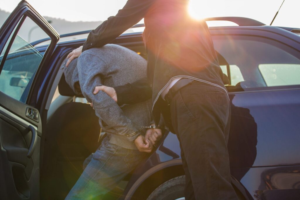 A man in handcuffs being put in a police car by a police officer. Representing how one can benefit from calling a Portland criminal defense attorney.