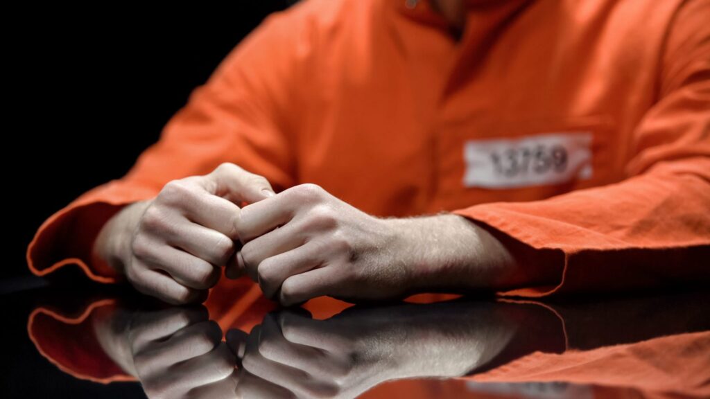 An inmate in an orange jumpsuit with his hands on a table, representing how one can benefit from calling a Portland criminal defense lawyer.
