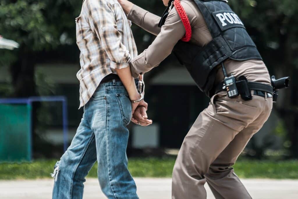 A man being walked in handcuffs by a police officer in a park, representing how one can benefit from calling a Portland criminal defense lawyer.