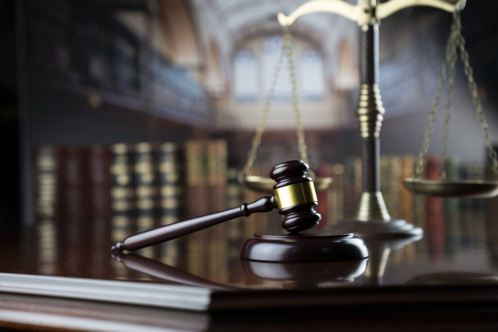 A judge's gavel resting on a block on top a table and there is a golden scale and books in the background, representing how one can benefit from calling a Portland criminal defense lawyer.