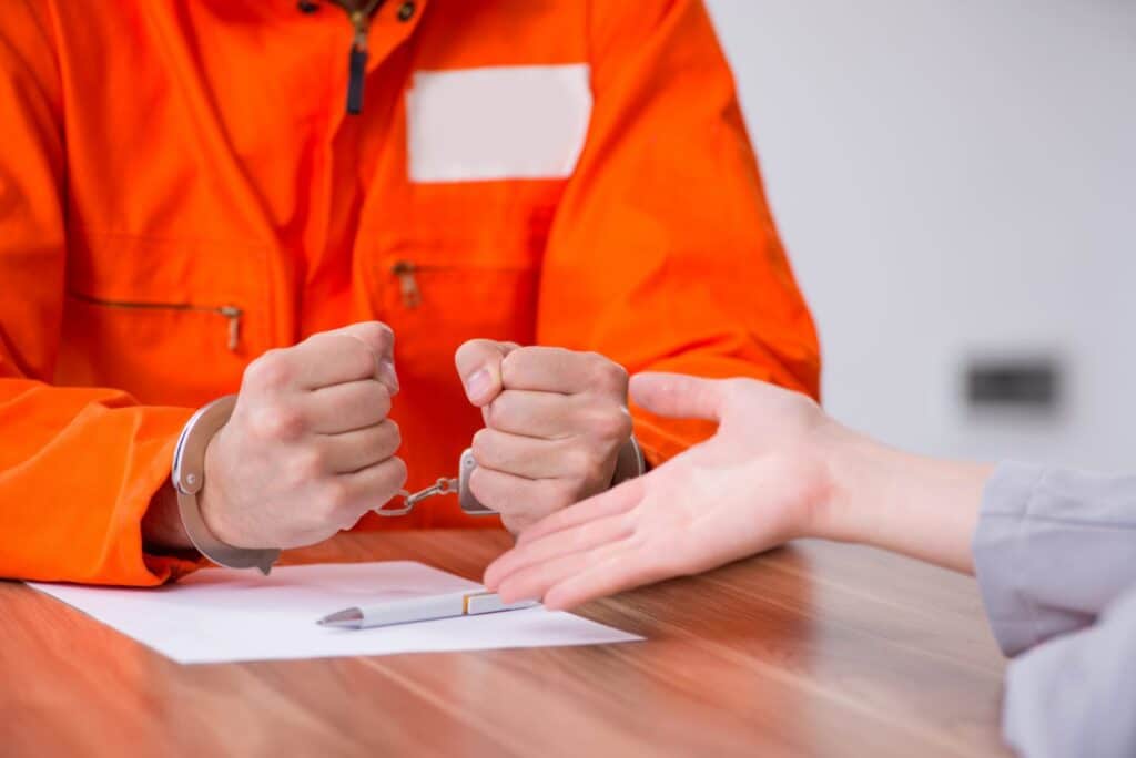 An inmate in handcuffs and a lawyer showing him a piece of paper, representing how one can benefit from calling a Portland criminal defense attorney.