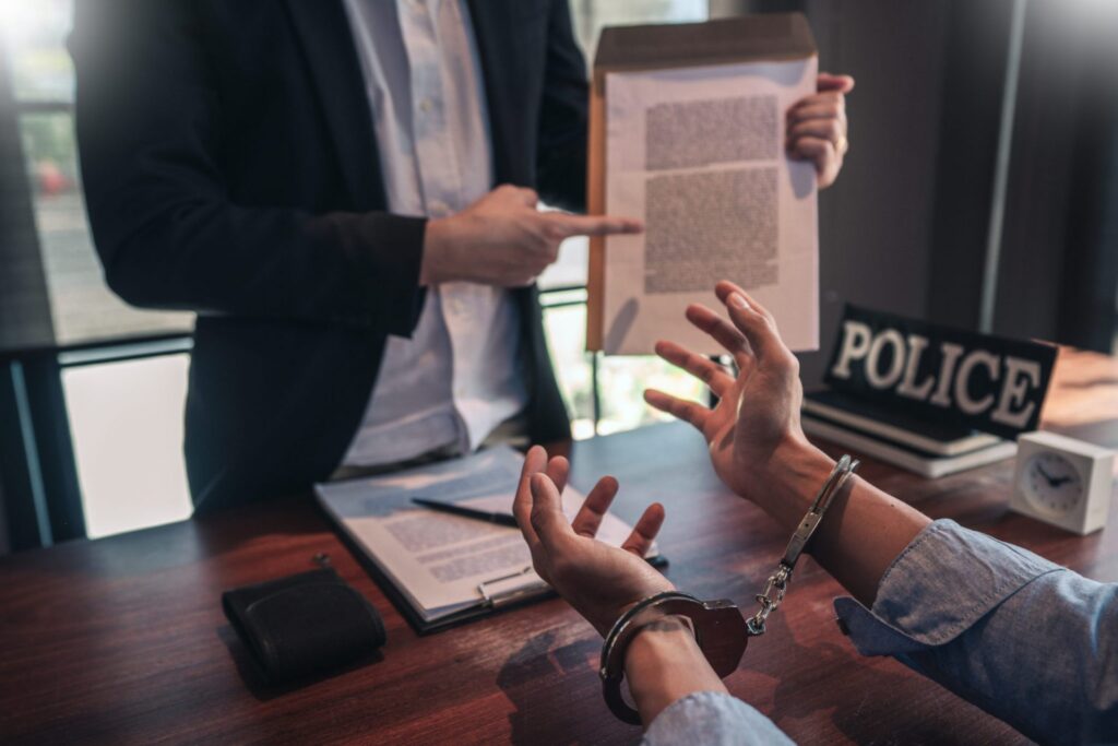A man in handcuffs and another man showing some paperwork, they are in an office. Representing how one can benefit from calling a Portland criminal defense attorney.