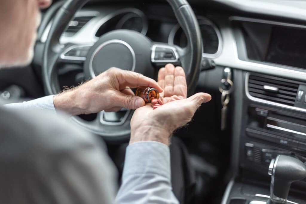 A man sitting on the driver's seat of a car, putting some orange pills in his hand, representing how one can benefit from calling a Portland criminal defense attorney.