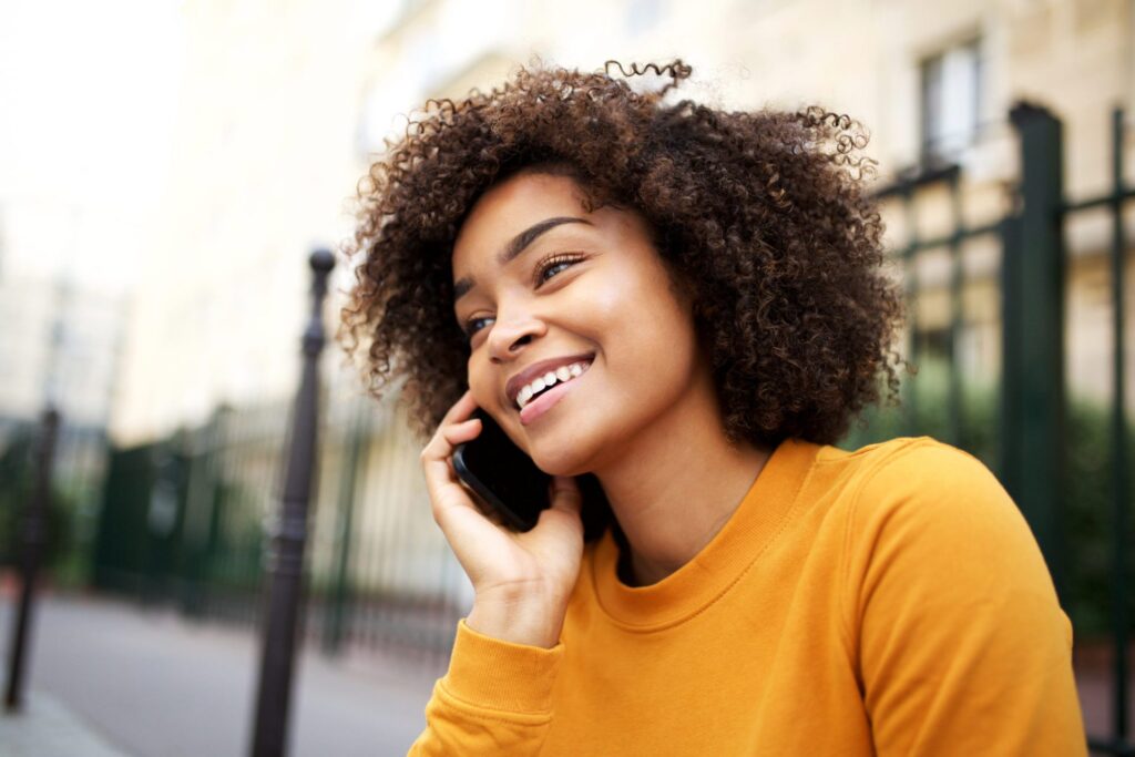 A woman wearing a yellow sweater taking a call from her cellphone, representing how one can benefit from calling a Portland criminal defense lawyer.