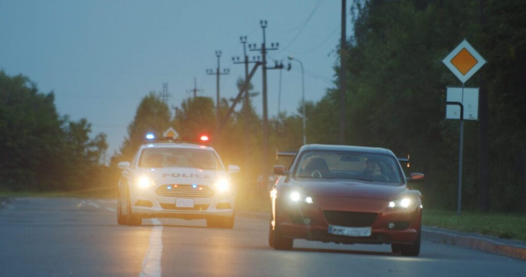 A police officer in car chasing a person driving a red car, representing how one can benefit from calling a Portland criminal defense lawyer.