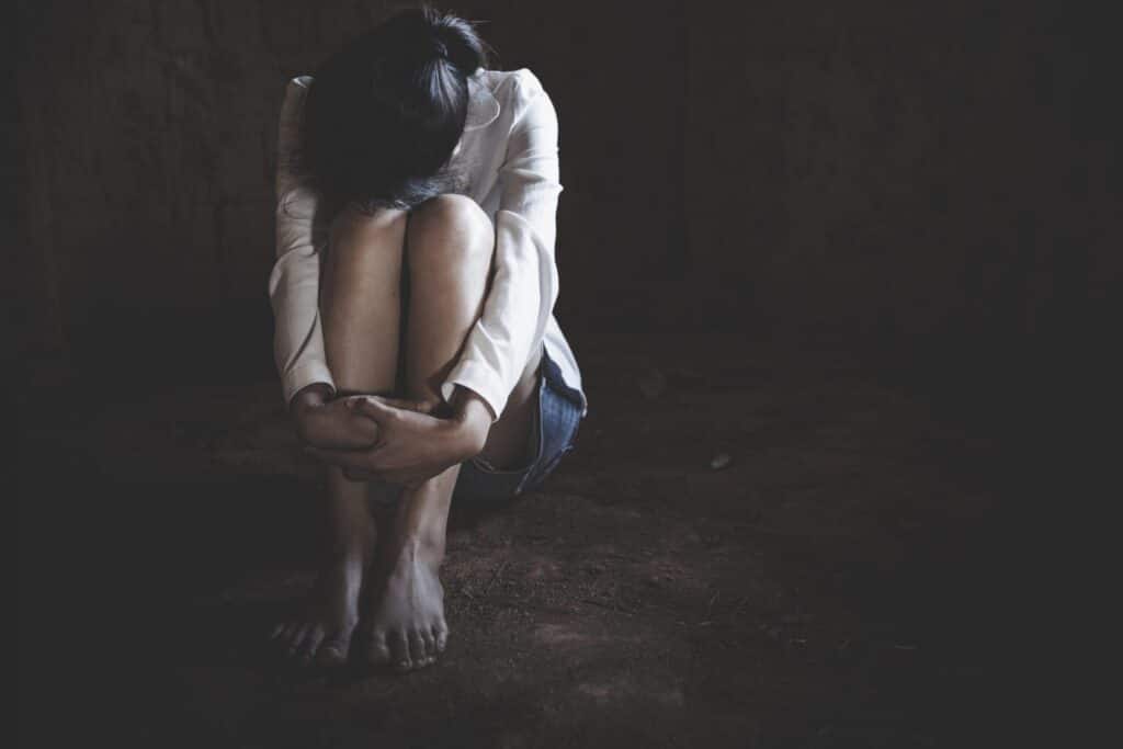 A young woman sitting on the floor hugging her knees and covering her face. Representing how one can benefit from calling a Portland criminal defense attorney.
