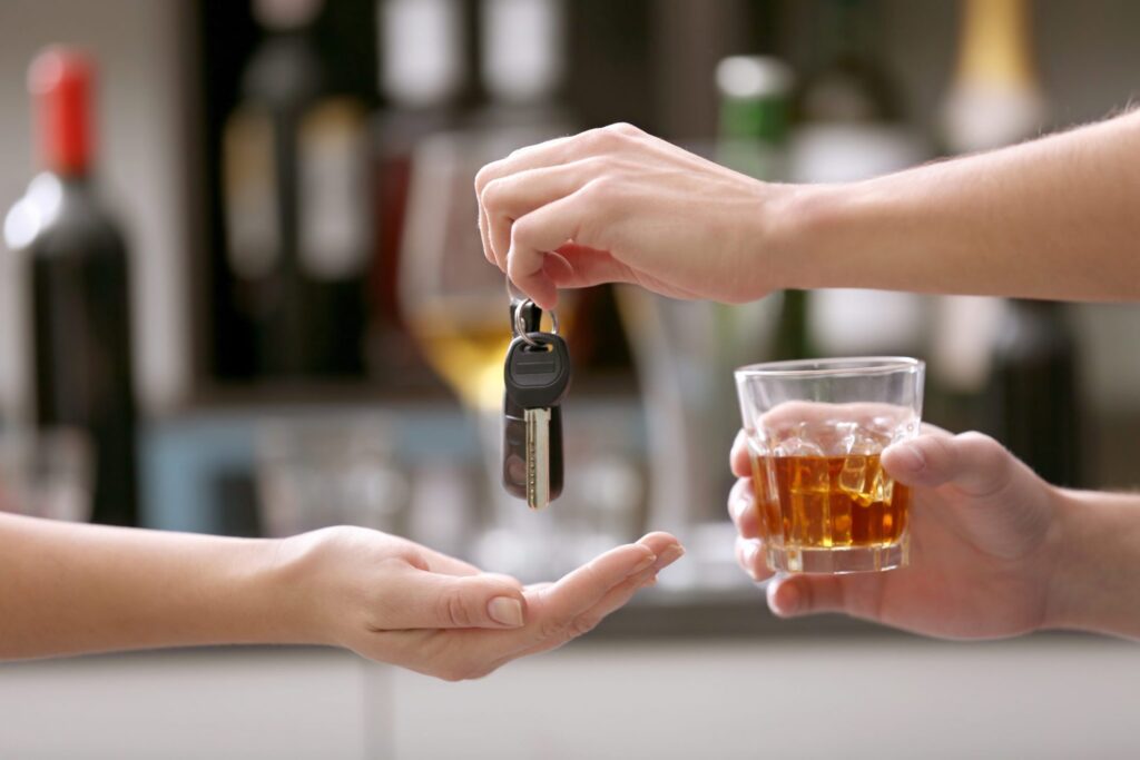A person holding an alcoholic beverage handing his car keys to somebody else at a bar, representing how one can benefit from calling a Portland criminal defense attorney.