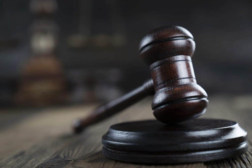 A wooden gavel and block on a table with books in the background, representing how one can benefit from calling a Portland criminal defense attorney.