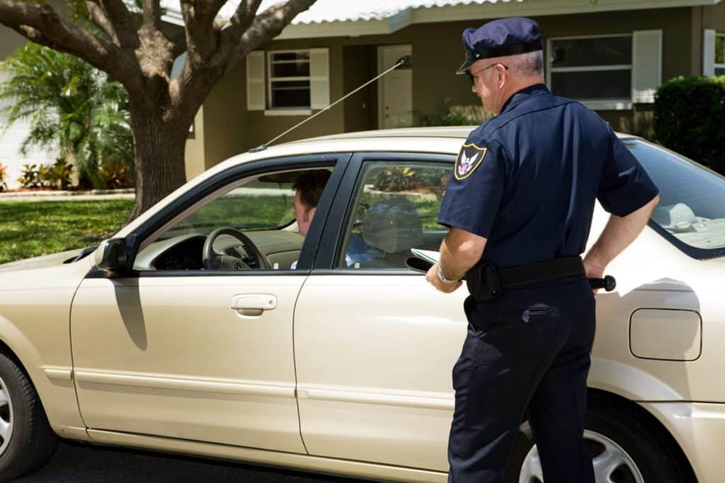 A police officer approaching a gold color car outside of a house, representing how one can benefit from calling a Portland criminal defense attorney.