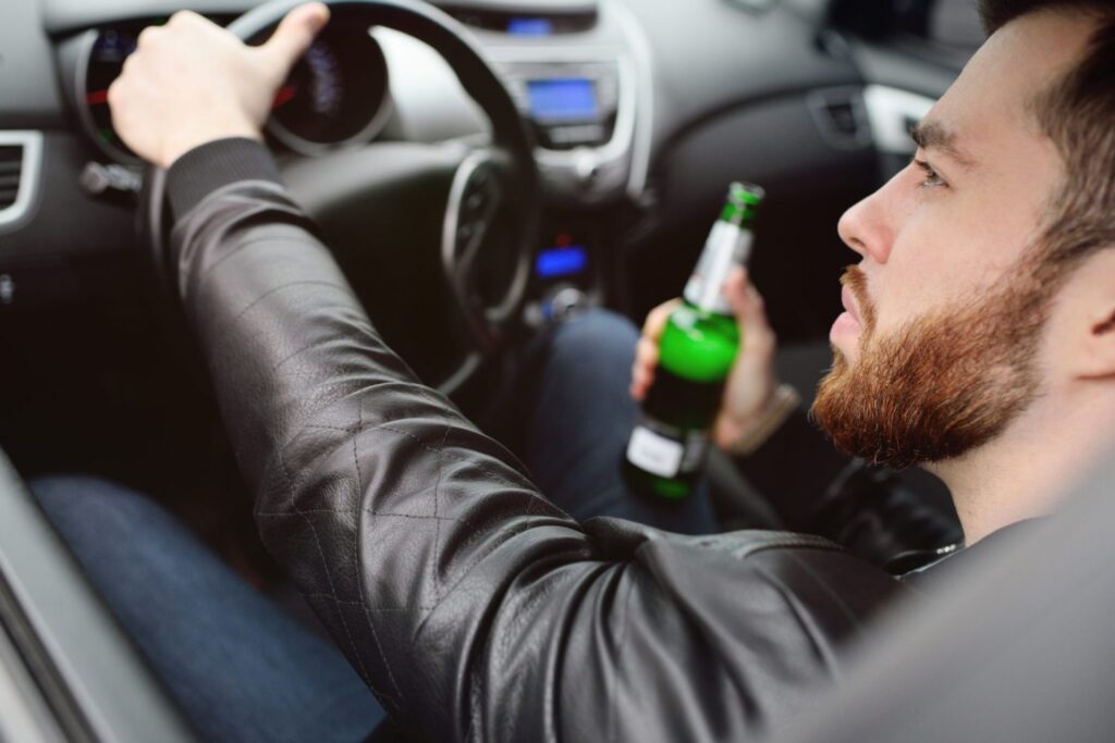 A man driving and drinking a beer at the same time, representing how one can benefit from calling a Portland criminal defense lawyer.