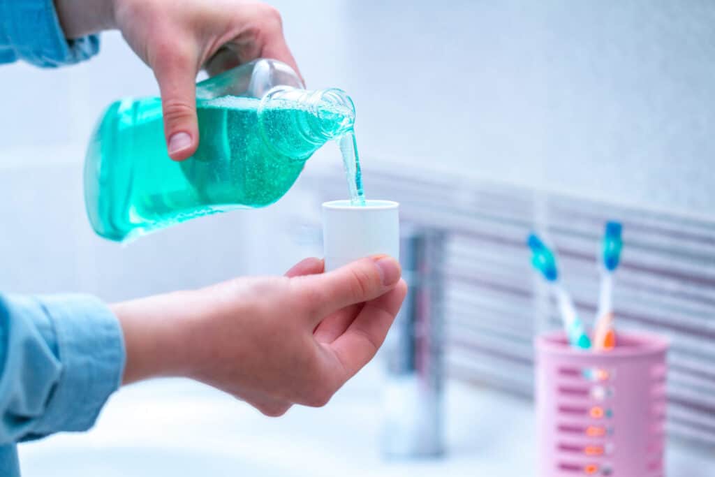 A man in a bathroom pouring some mouthwash into the cap, representing how one can benefit from calling a Portland criminal defense lawyer.