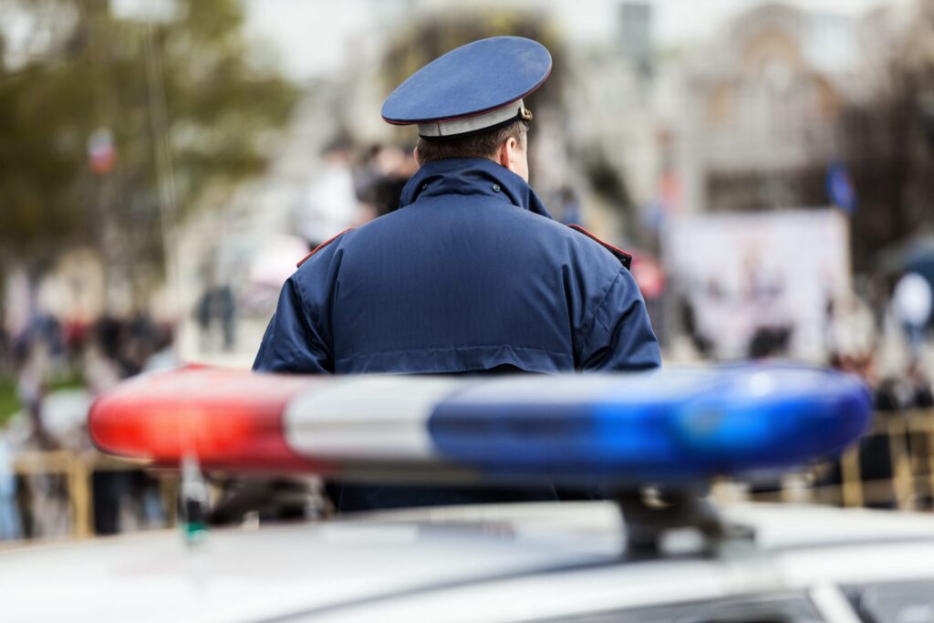 A police officer walking and his police car is parked, representing how one can benefit from calling a Portland criminal defense attorney.