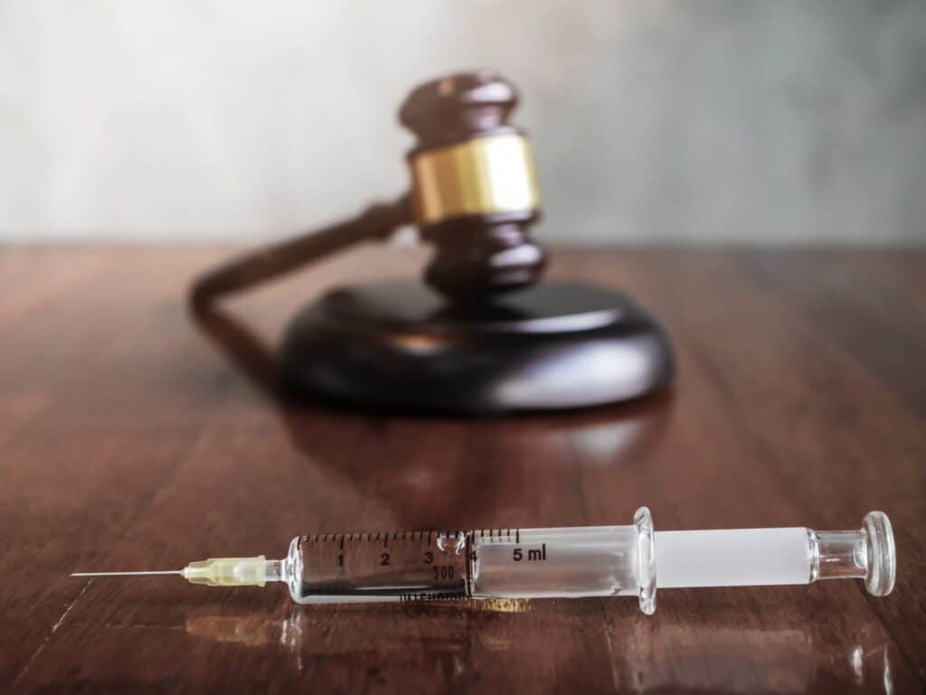 A needle with some medical liquid in it and a judge's gavel and block, representing how one can benefit from calling a Portland criminal defense lawyer.