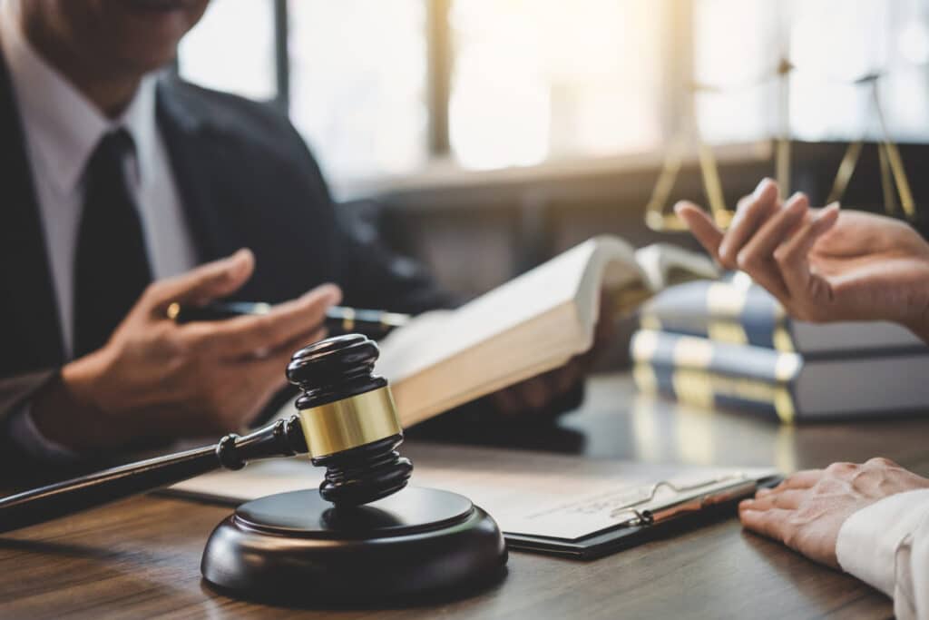 A lawyer explaining something to a client in a desk, there is gavel resting on a block representing how one can benefit from calling a Portland criminal defense lawyer.