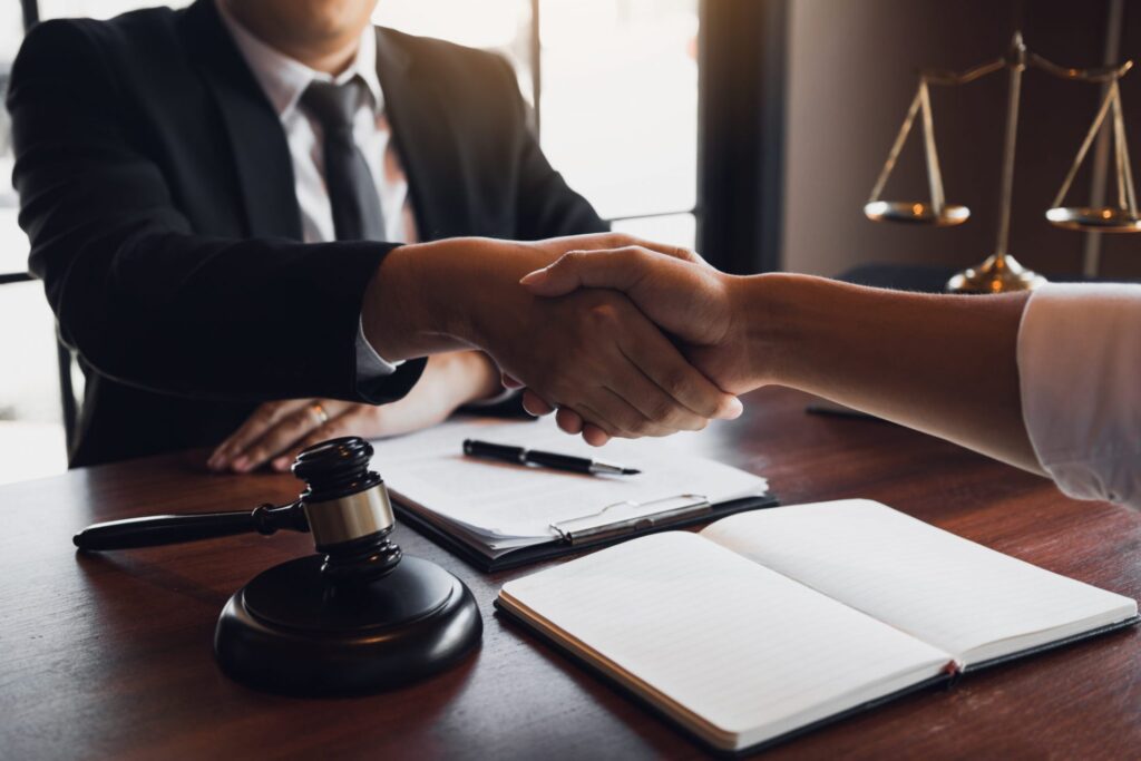 A judge shaking hands with somebody over a table with paper work and gavel, representing how one can benefit from calling a Portlad criminal defense lawyer.