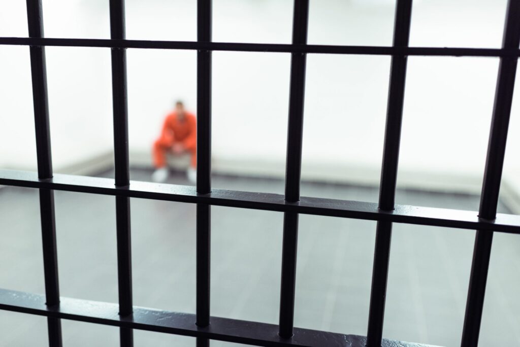 A man wearing an orange jumpsuit sitting in a jail cell, representing how one can benefit from calling a Portland criminal defense lawyer.
