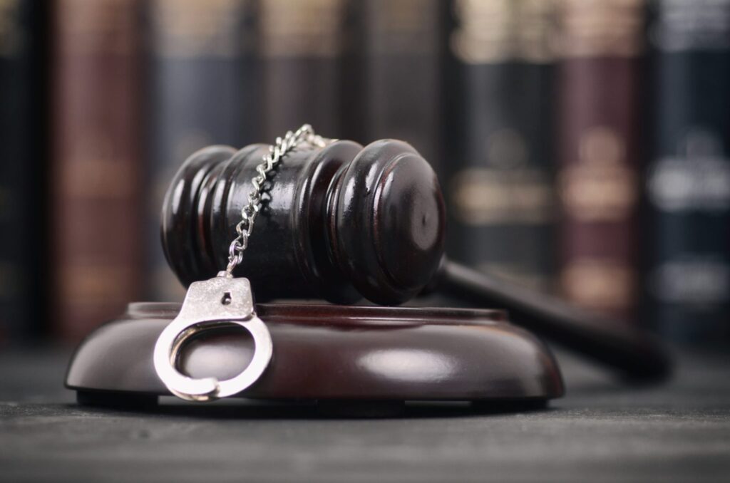 A judge's gavel with a set of handcuffs on top with books in the background, representing how one can benefit from calling a Portland criminal defense lawyer.