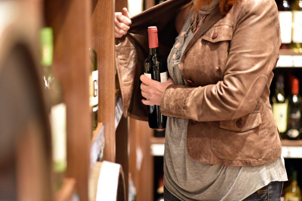 A woman in a store putting a bottle of wine under her coat, representing how one can benefit from calling a Portland criminal defense lawyer.