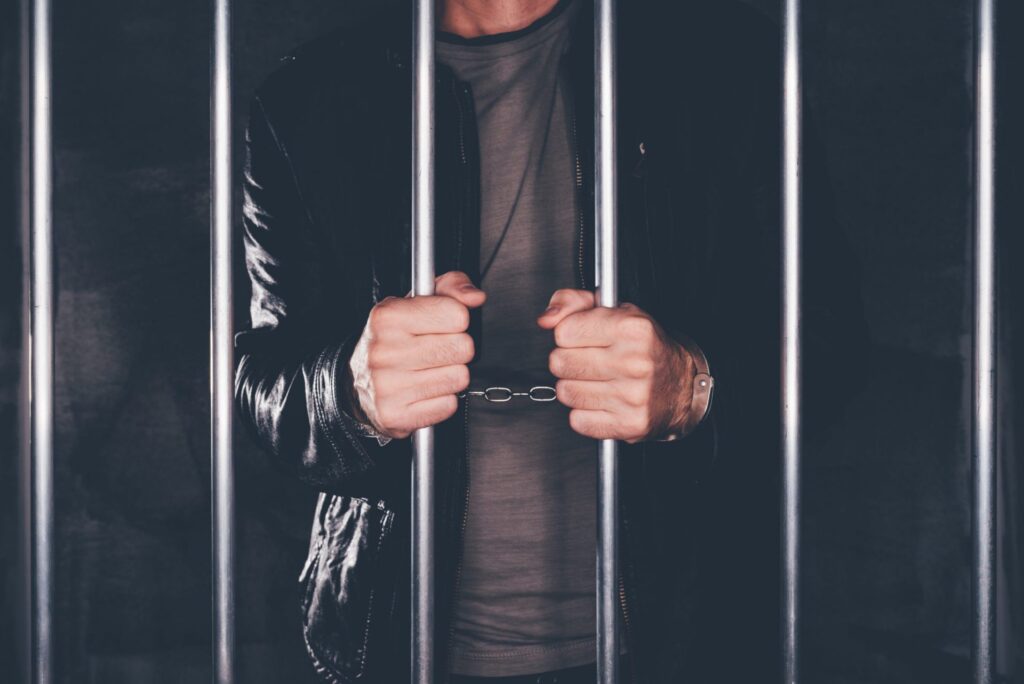 A man in jail holding the cells with his hands, representing how one can benefit from calling a Portland criminal defense lawyer.