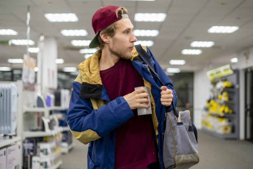 A man wearing a cap walking in a store putting something in his jacket while he looks around, representing how one can benefit from calling a Portland criminal defense lawyer.