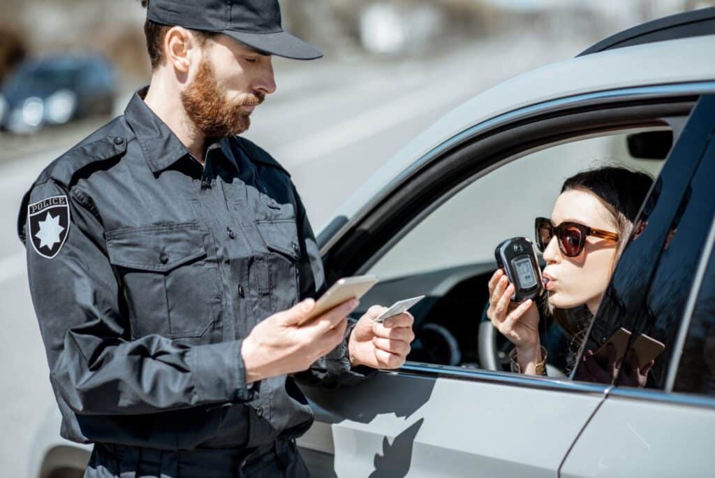 A police officer performing a breath test to a woman in a silver car, representing how one can benefit from calling a Portland criminal defense lawyer.