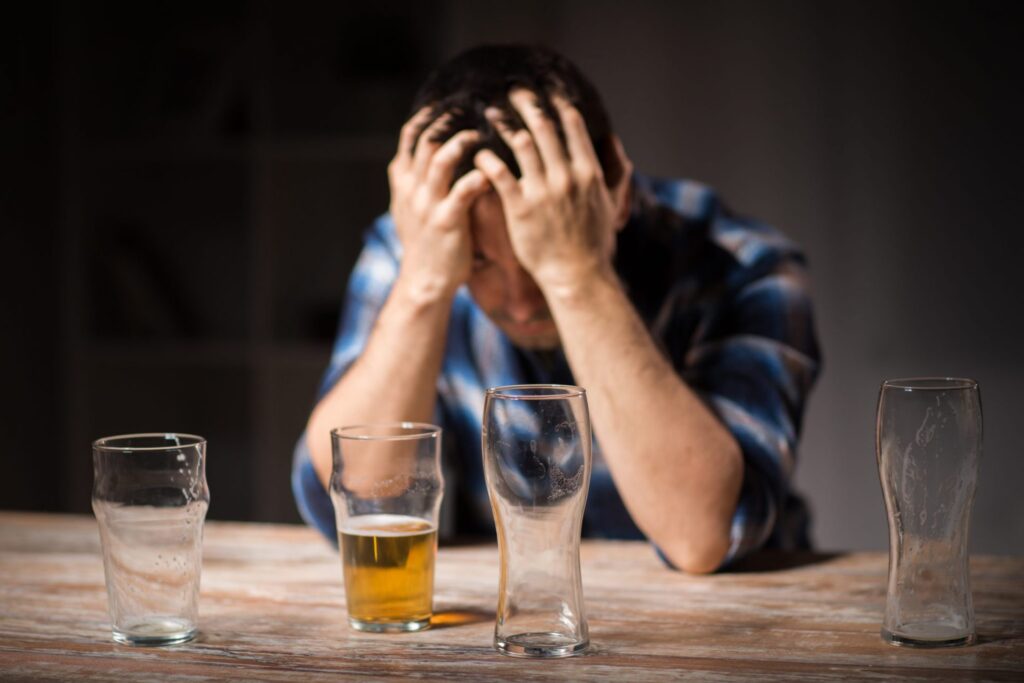 A man with his hands over his head, empty glasses in front of him and one still half full of beer, representing how one can benefit from calling a Portland criminal defense lawyer.