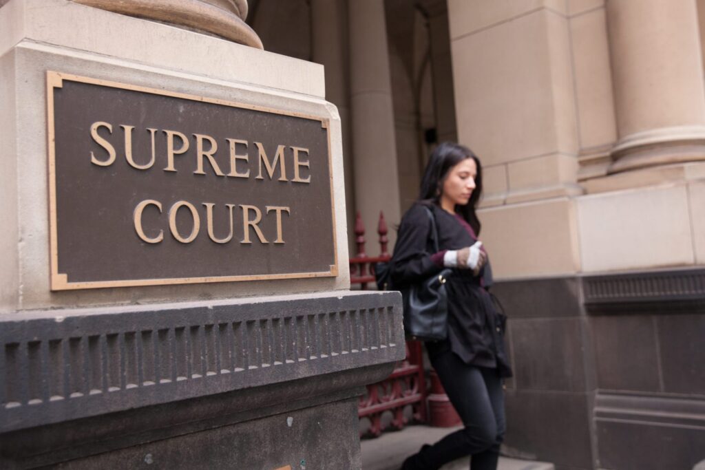 The outside of the Supreme Court and woman walking out of there, representing how one can benefit from calling a Portland criminal defense lawyer.