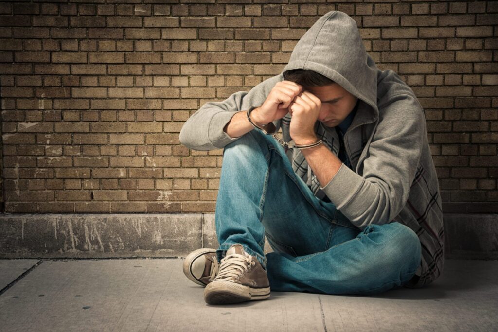 A teenager wearing a hoodie is against a wall wearing handcuffs, representing how one can benefit from calling a Portland criminal defense lawyer.