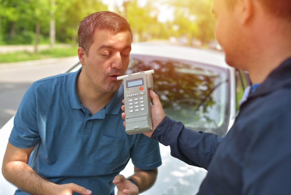 A policeman giving a breath test to a man outside his car, representing how one can benefit from calling a Portland criminal defense lawyer.