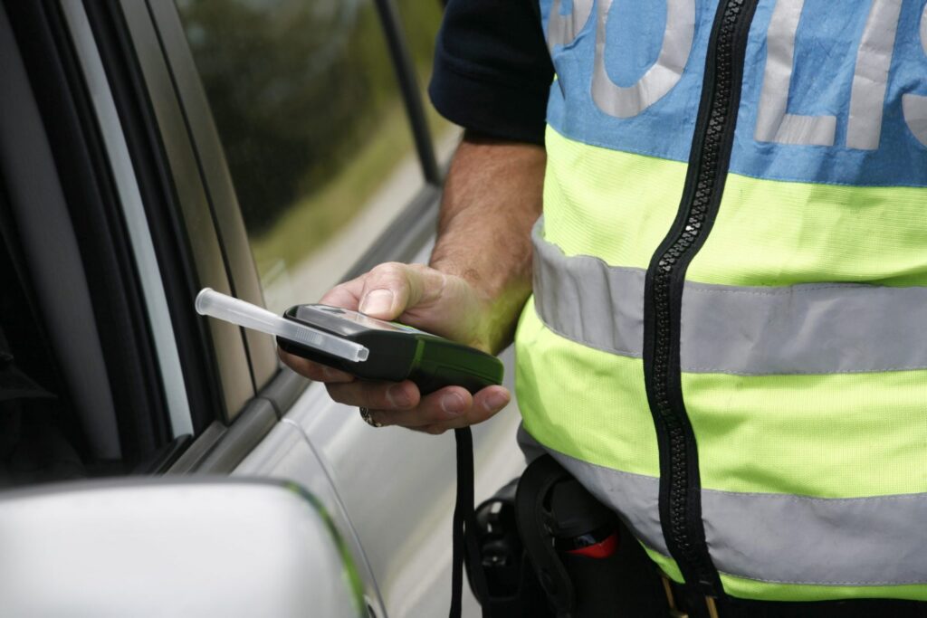 A policer officer holding a breathalyzer approaching a car, representing how one can benefit from calling a Portland criminal defense attorney.