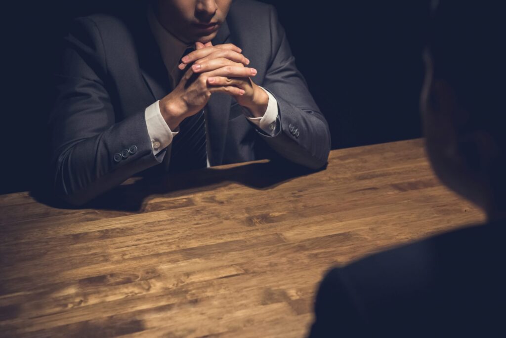 A man being questioned by another person sitting at a table, representing how one can benefit from calling a Portland criminal defense lawyer.