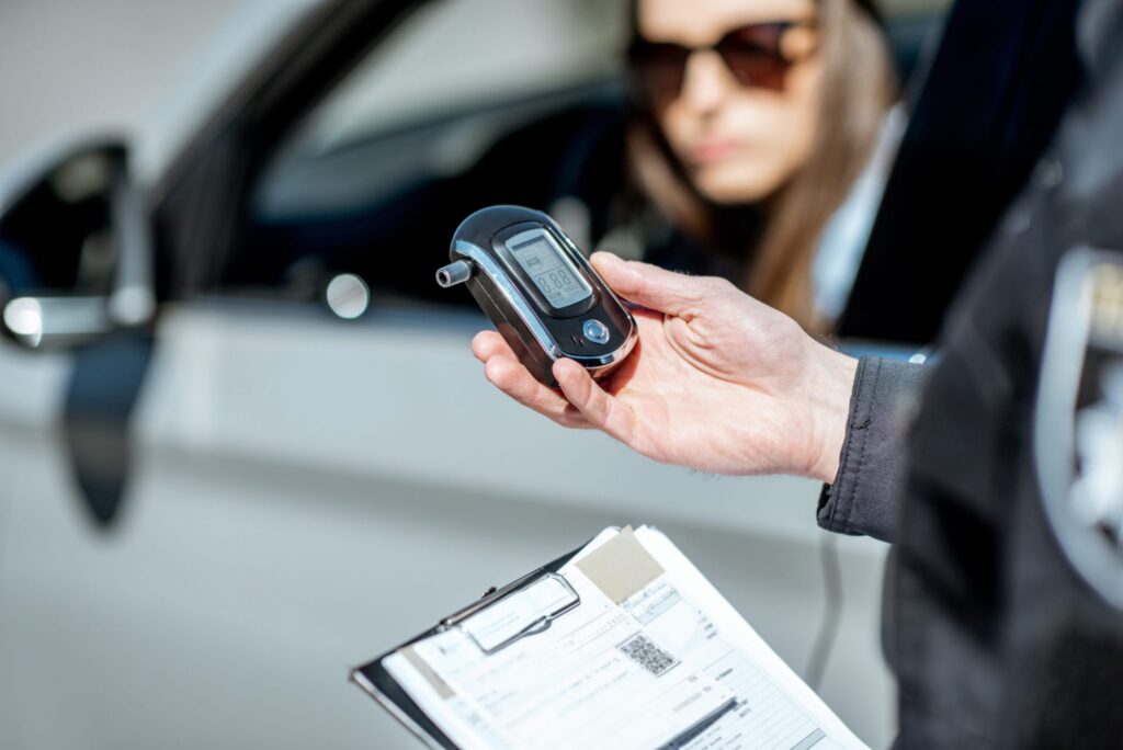 A policeman with a breathlyzer approaching a women in a car, representing how one can benefit from calling a Portland criminal defense lawyer.