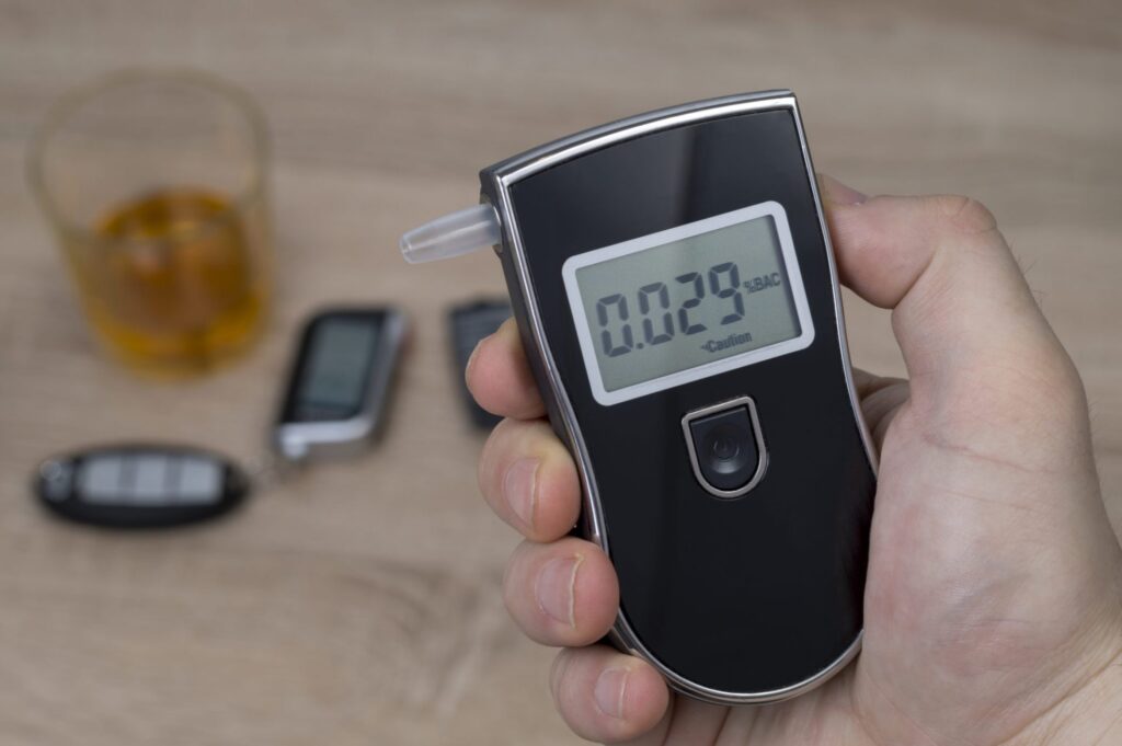 A person holding a breathlyzer and there is a set of car keys and an alcoholic drink the background, representing how one can benefit from calling a Portland criminal defense lawyer.