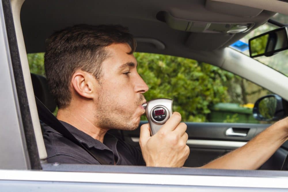 A man blowing into a breathlyzer inside of a car, representing how one can benefit from calling a Maine criminal defense lawyer.