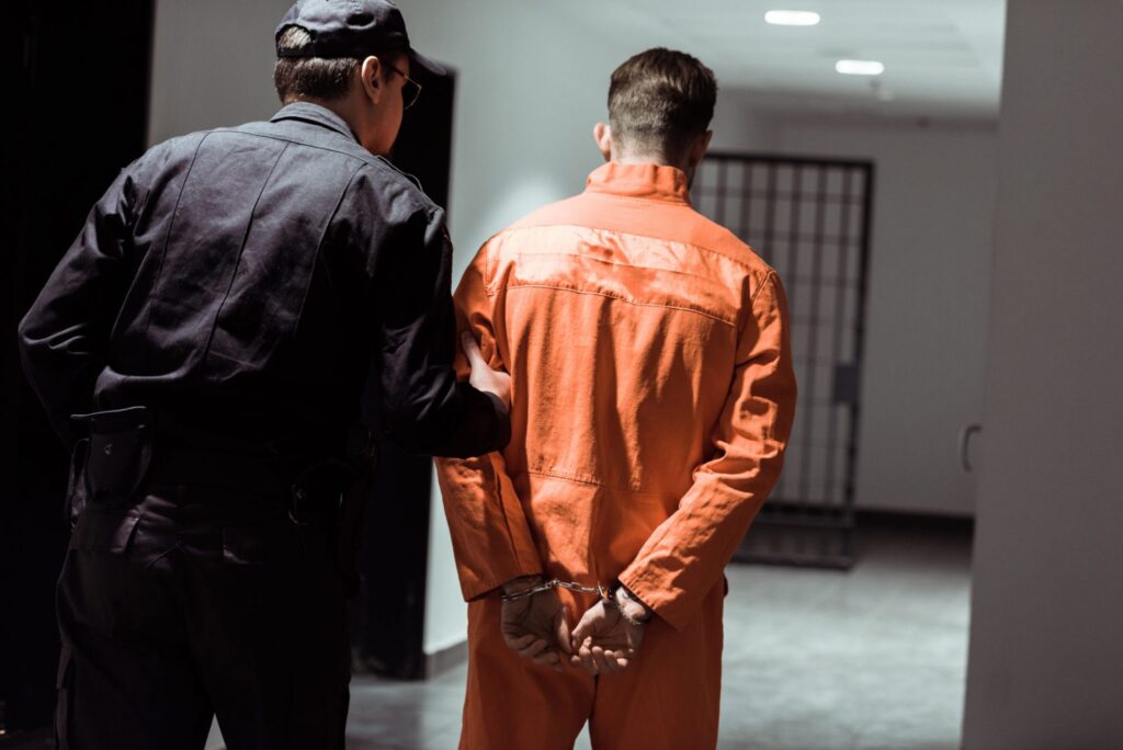 An officer walking an inmate with handcuffs to his cell, representing how one can benefit from calling a Portland criminal defense attorney.