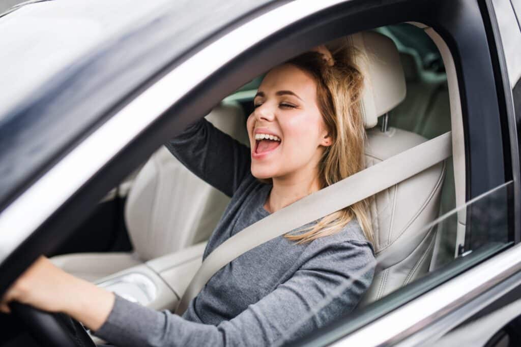 A woman driving, she is singing and her eyes are close, representing how one can benefit from calling a Portland criminal defense lawyer.