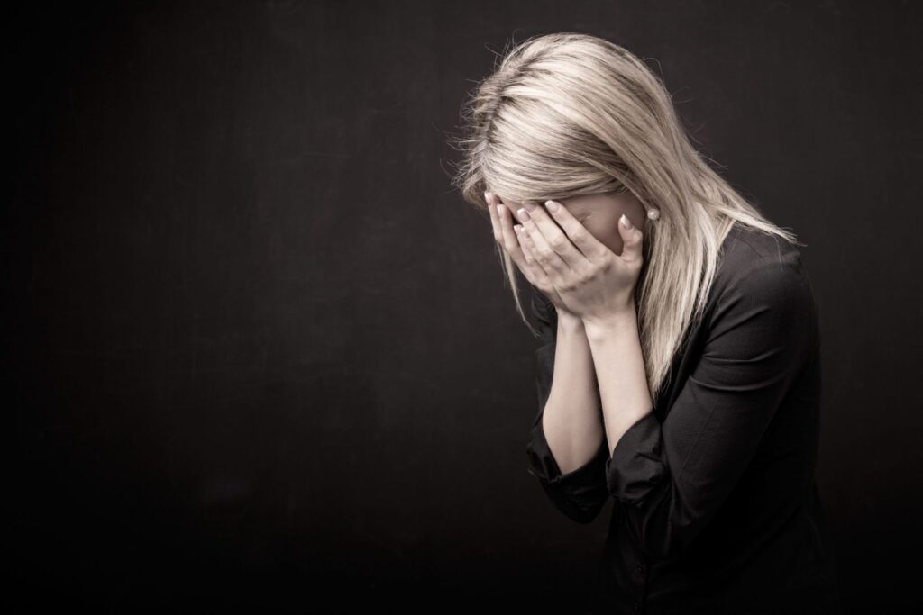 A woman covering his face it seems like she is crying, representing how one can benefit from calling a Portland criminal defense lawyer.