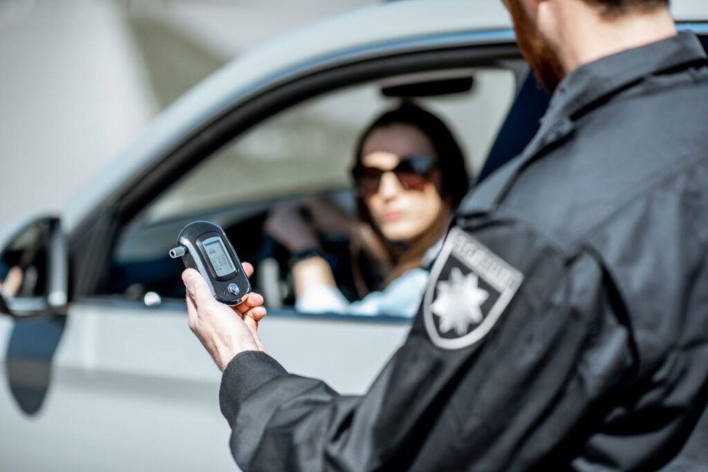 A police offer with a breathalyzer approaching a women in a car, representing how one can benefit from calling a Portland criminal defense lawyer.