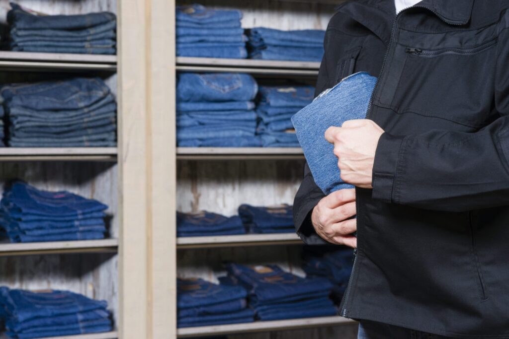 A man putting a pair of jeans inside his coat, making it seem like he is shoplifting representing how one can benefit from calling a Portland criminal defense lawyer.