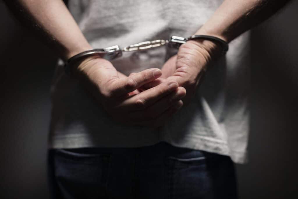 A man wearing a white shirt with his hands behind his back on handcuffs representing how one can benefit from calling a Portland criminal defense lawyer.