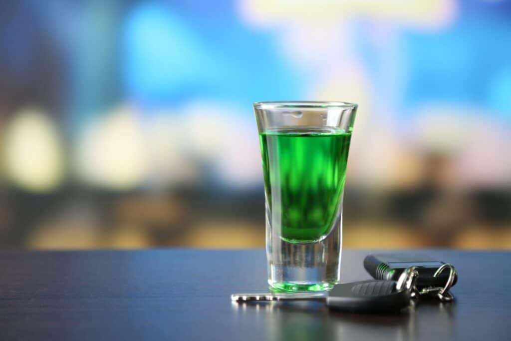A glass with a green alcoholic drink and a set of car keys next to it, representing how one can benefit from calling a Portland criminal defense lawyer.