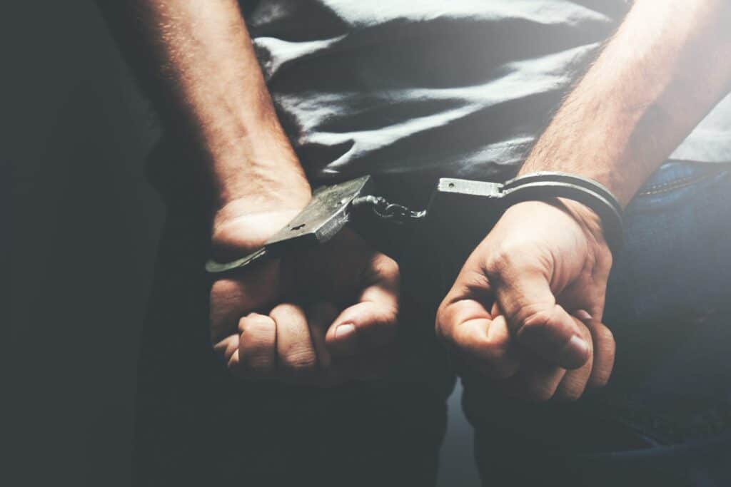 A man with his hands in handcuffs behind his back, representing how one can benefit from calling a Maine criminal defense lawyer.