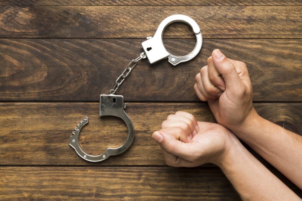 A set of of hands on a table facing a pair of handcuffs, representing how one can benefit from calling a Portland criminal defense lawyer.